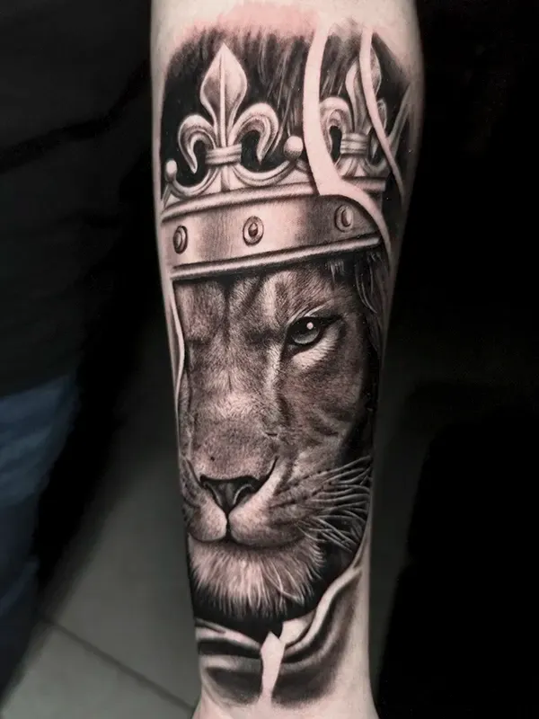 Tatuaje realista de león con corona en antebrazo terminado por Clayton Goethe